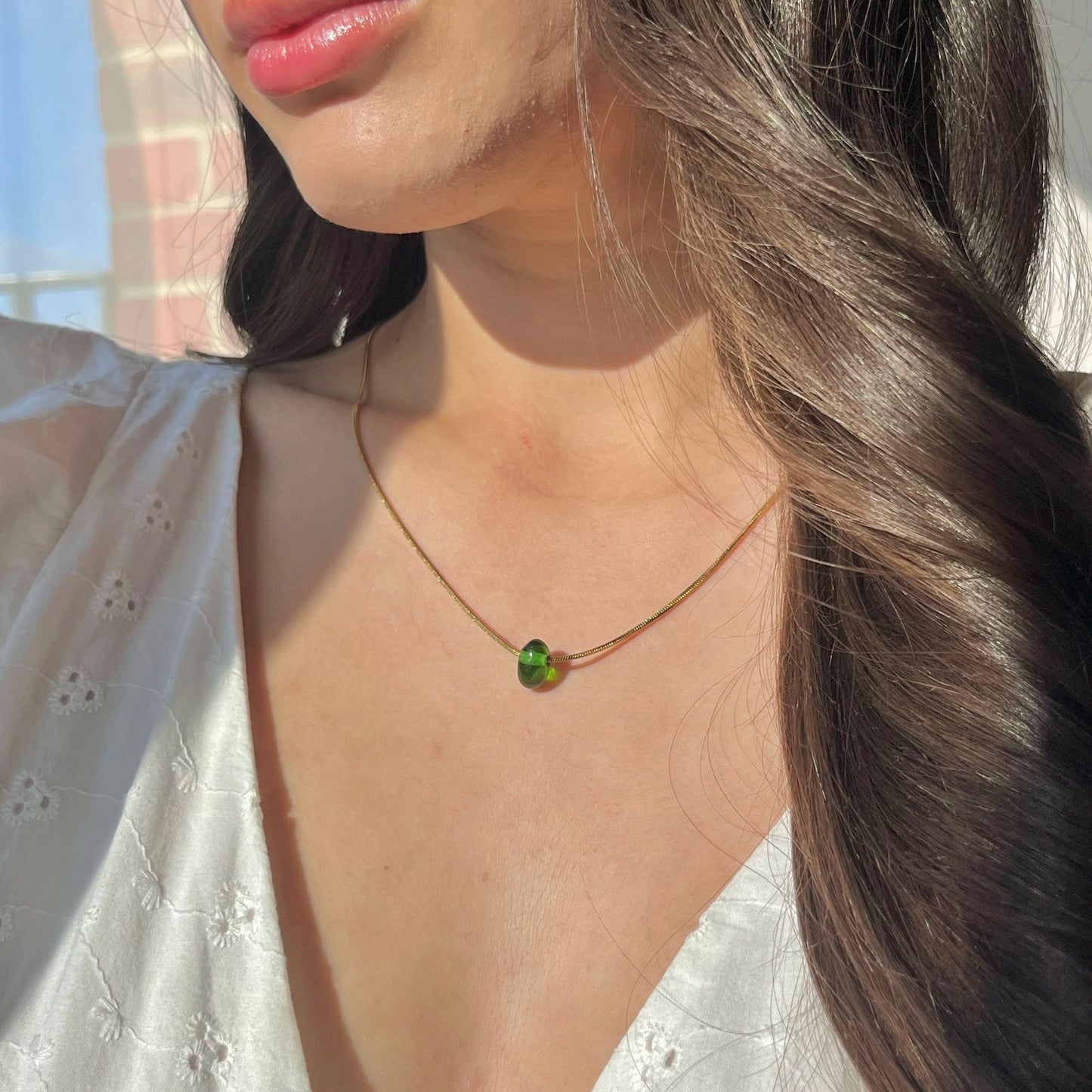 Close-up of a person wearing a necklace with a green pendant, outdoors.