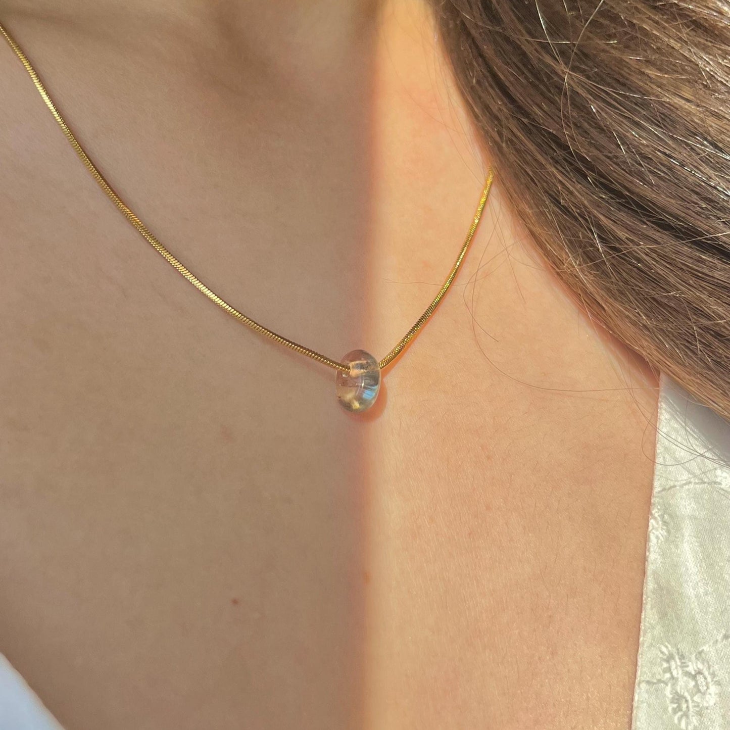 Gold necklace with a single bead on a person's neck