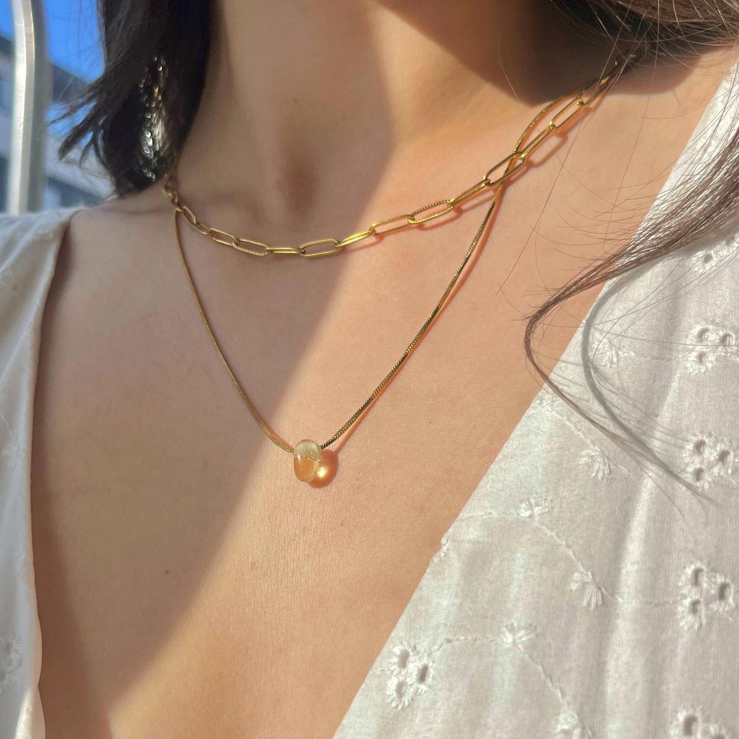 Close-up of a gold chain necklace with a pendant on a person wearing a white top.