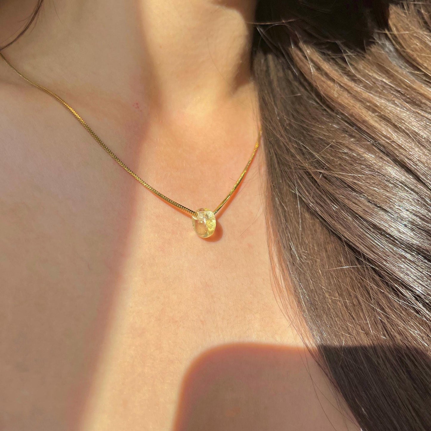 
                  
                    Gold necklace with a yellow gemstone on a person's neck
                  
                