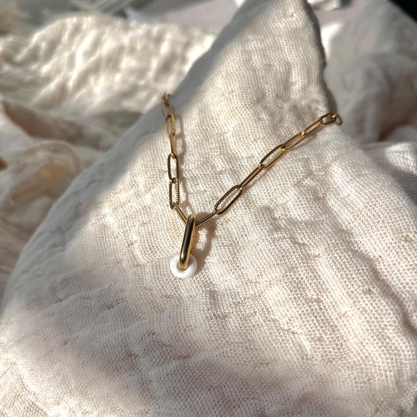 
                  
                    Gold chain necklace on a textured beige fabric background
                  
                