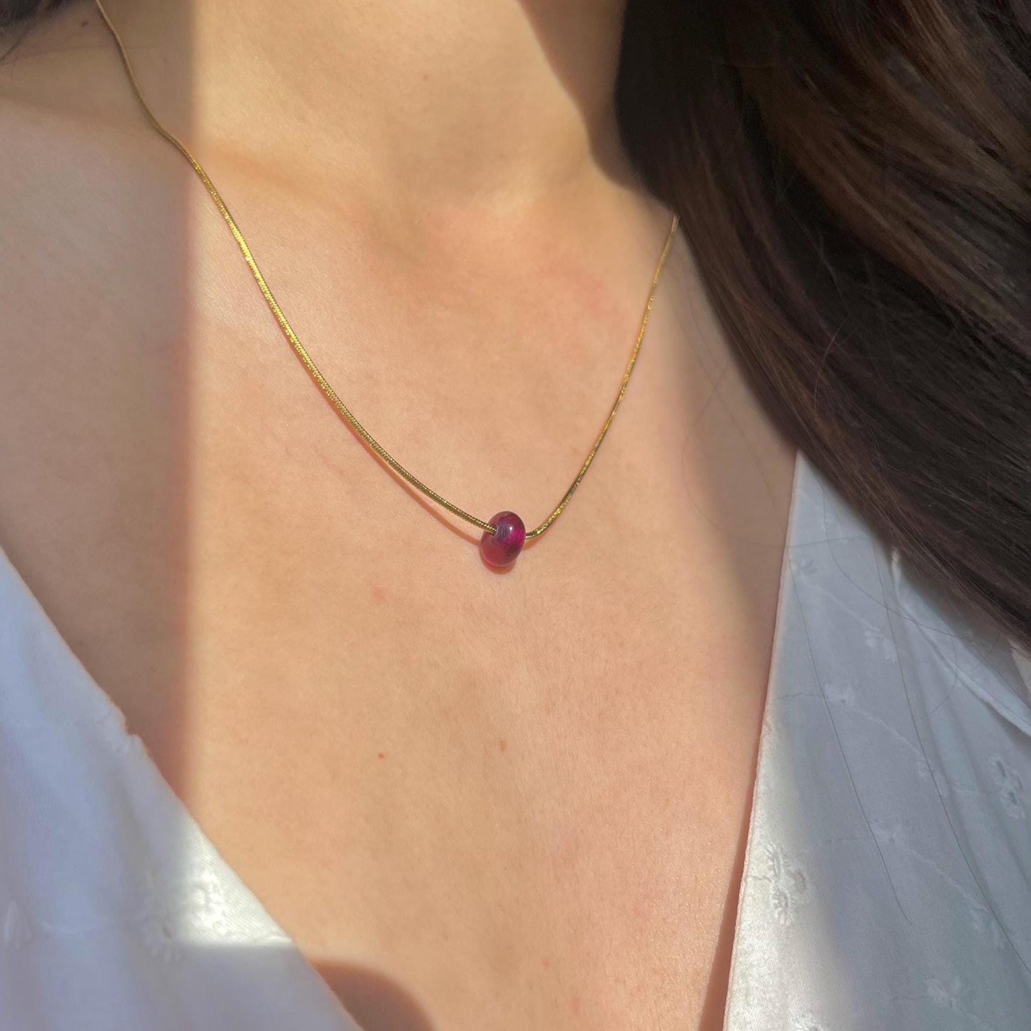 Necklace with a red gemstone on a person wearing a white top.