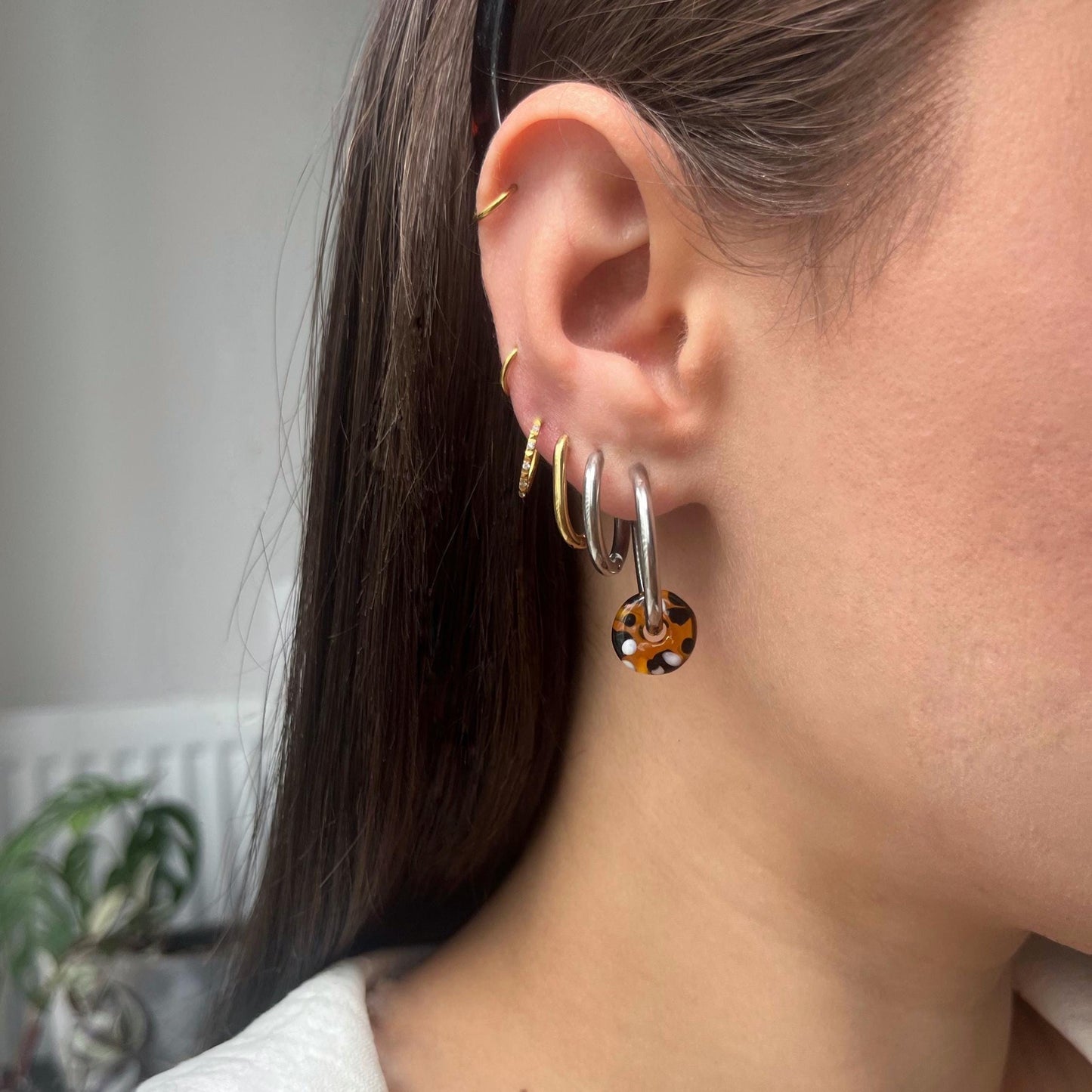 
                  
                    Close-up of an ear with multiple earrings against a neutral background
                  
                