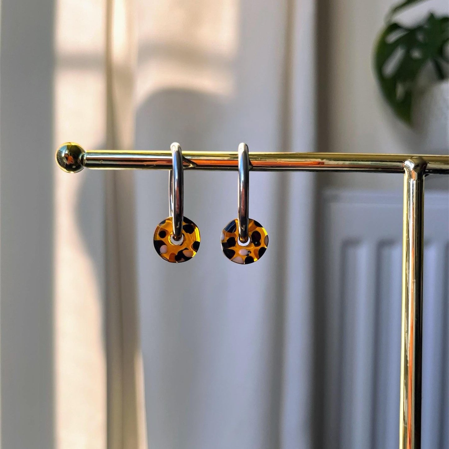 Pair of earrings with leopard print charms on a gold stand against a neutral background