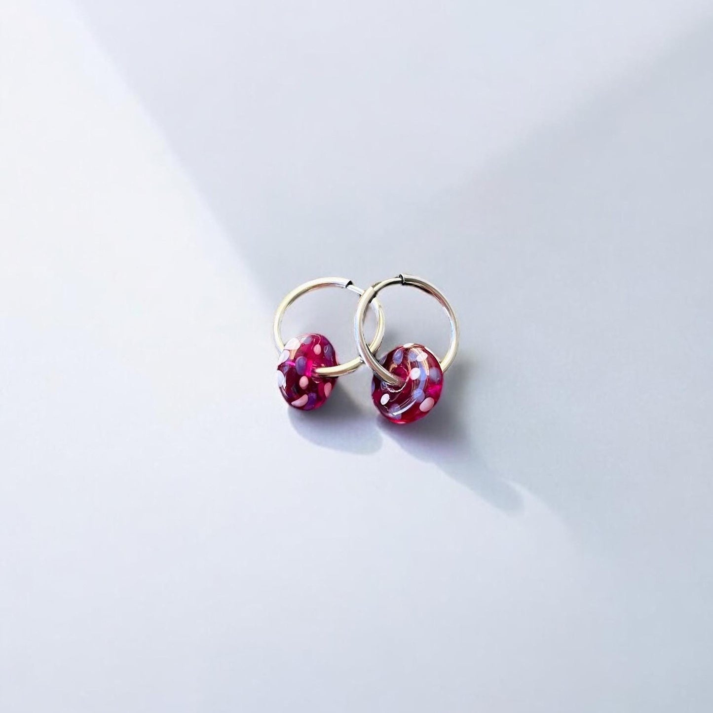 Gold hoop earrings with red gemstones on a light gray background