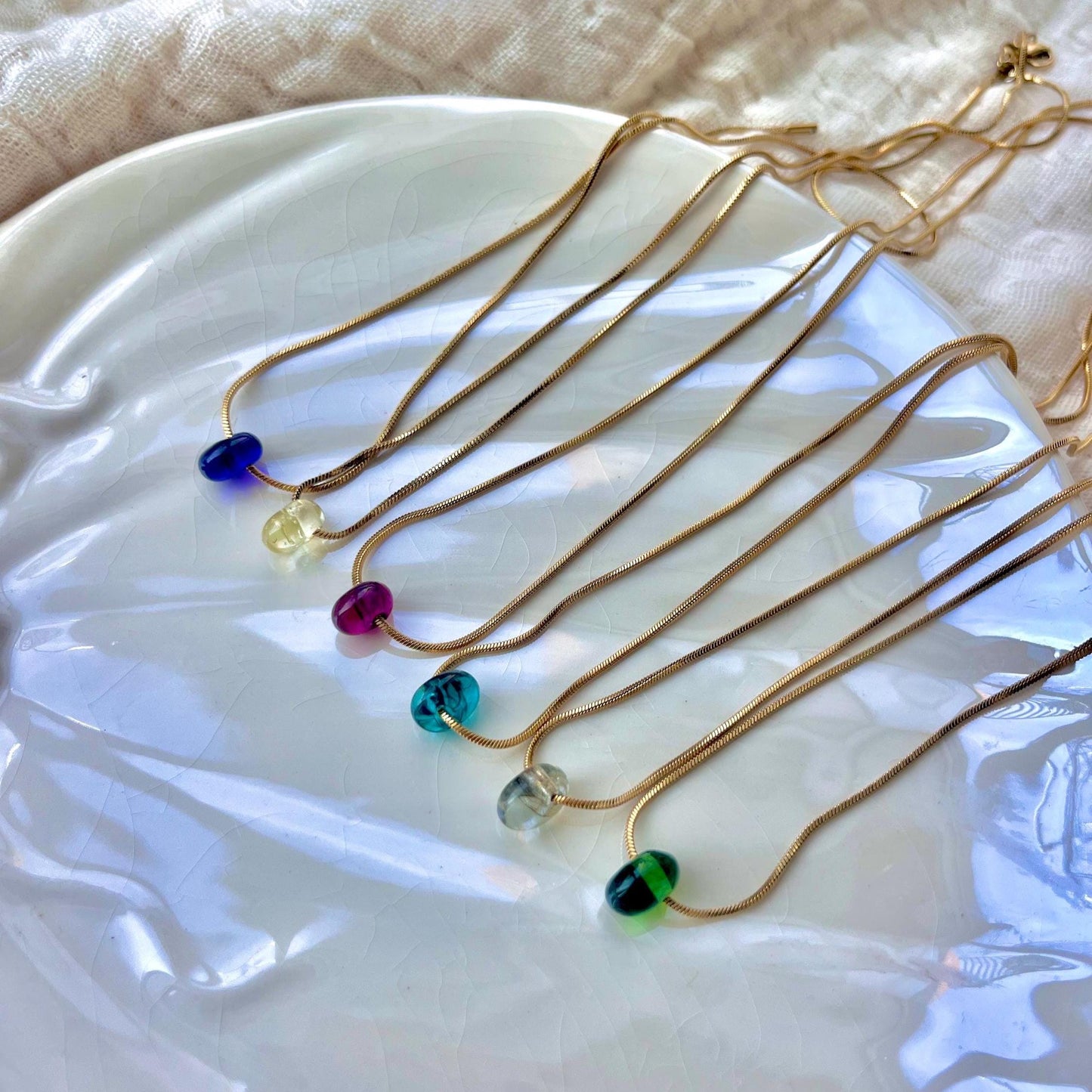 
                  
                    Set of gold necklaces with colorful beads on a white dish
                  
                