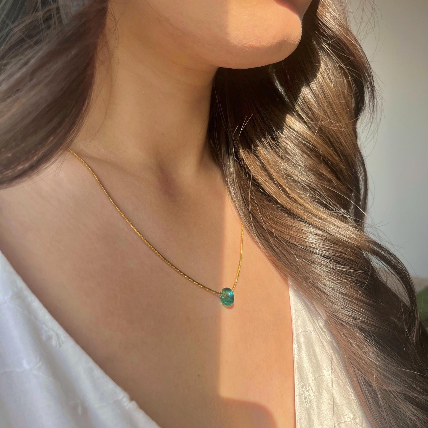 
                  
                    Close-up of a person wearing a gold necklace with a green pendant.
                  
                