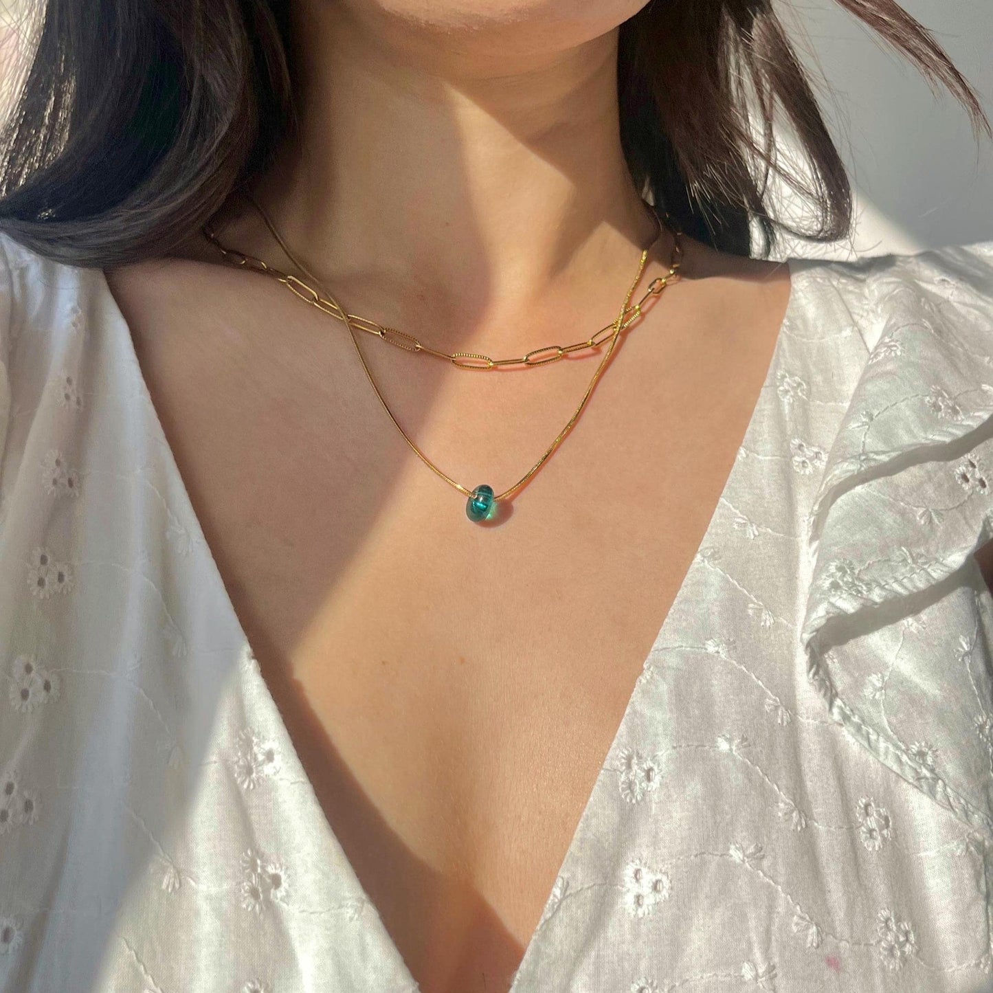 Close-up of a person wearing a gold necklace with a green gemstone on a white background