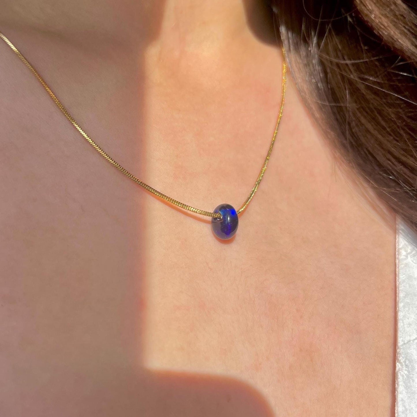 
                  
                    Gold necklace with a blue pendant on a person's neck
                  
                