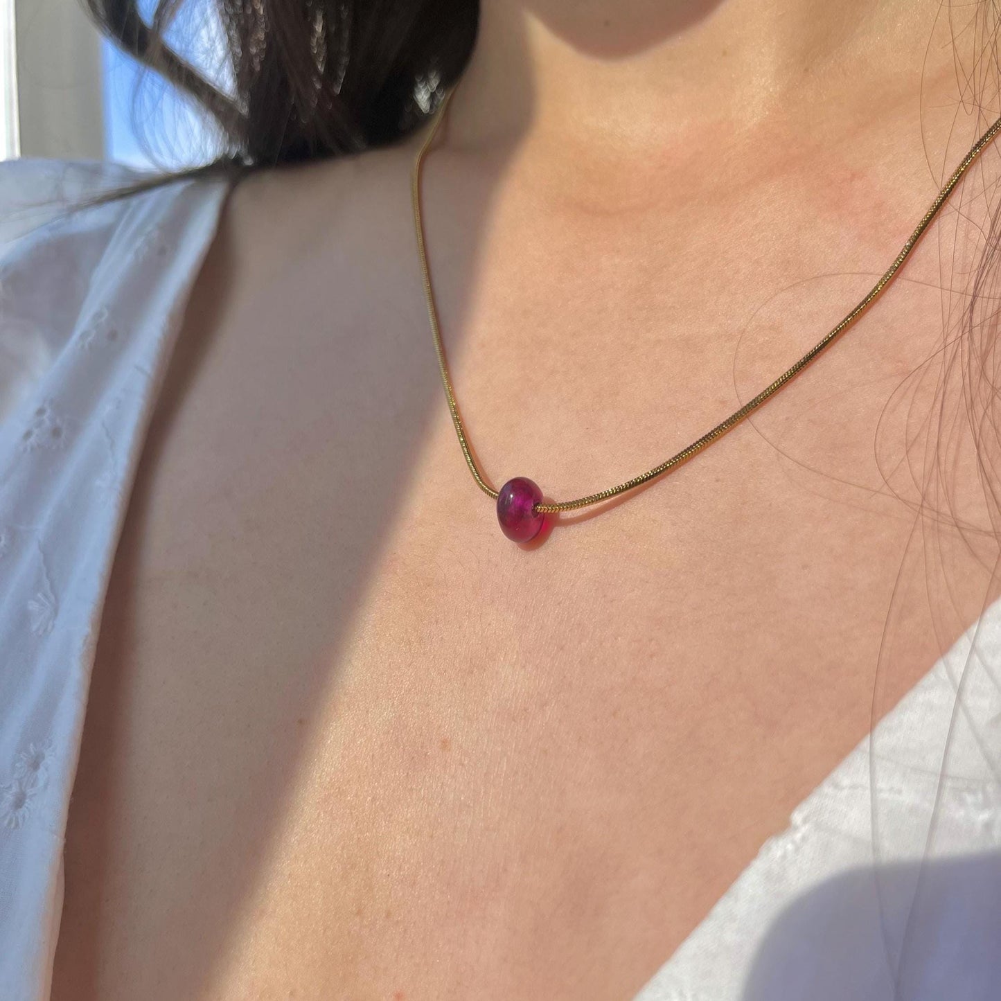 Necklace with a red bead worn by a person in a white shirt.
