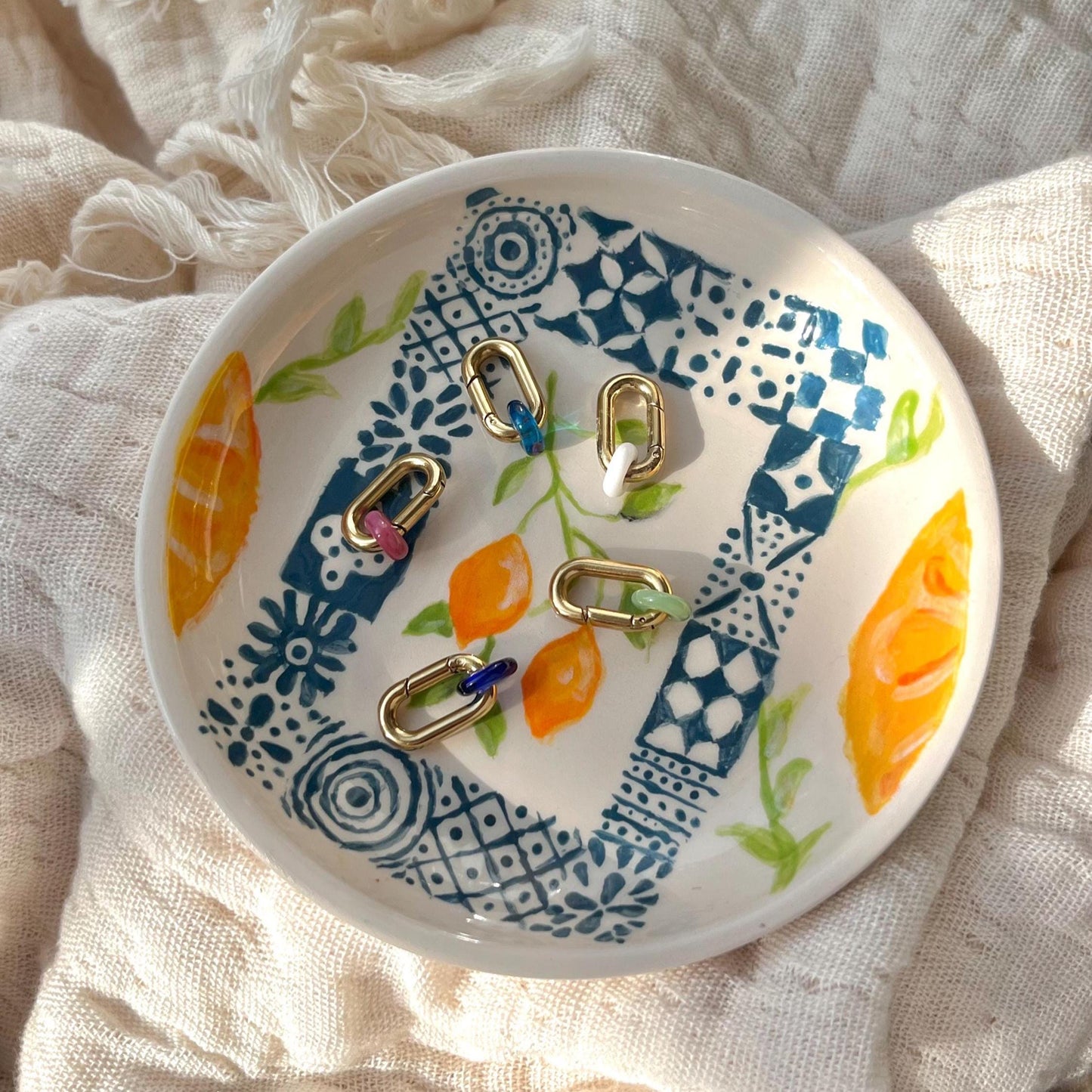
                  
                    Decorative ceramic dish with floral patterns and jewelry on a textured fabric background
                  
                