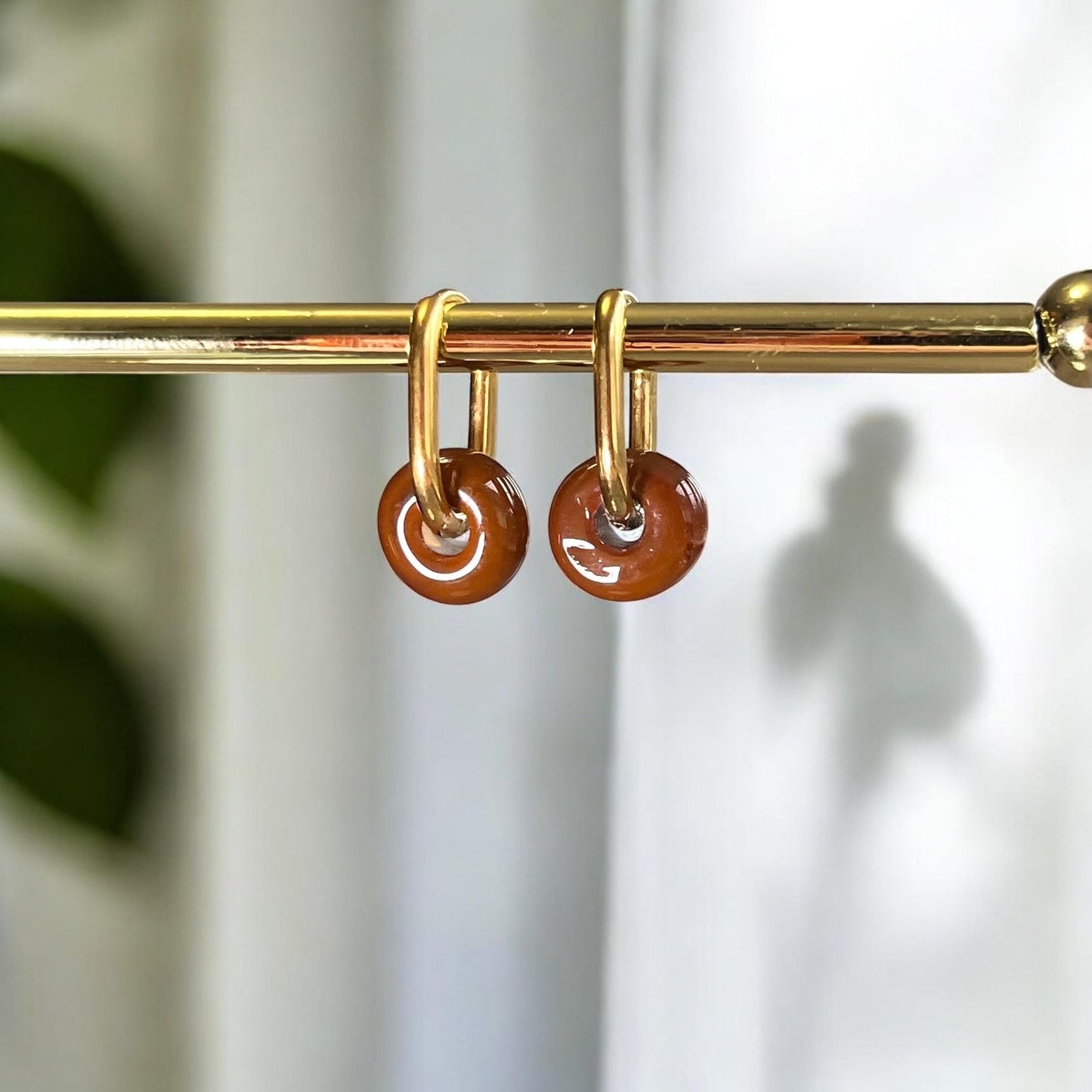 
                  
                    Gold earrings with brown circular charms on a gold rod against a blurred background
                  
                