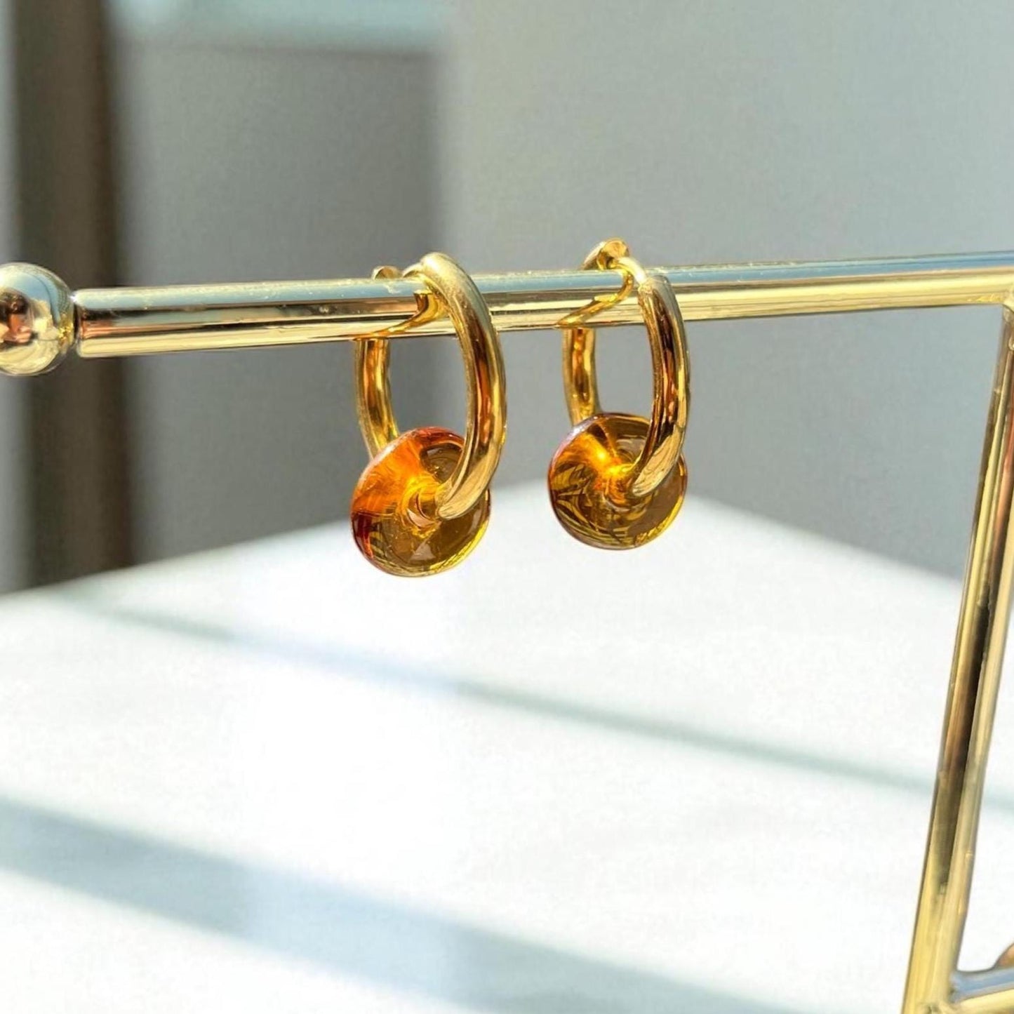 Gold hoop earrings with amber-colored beads on a gold stand.