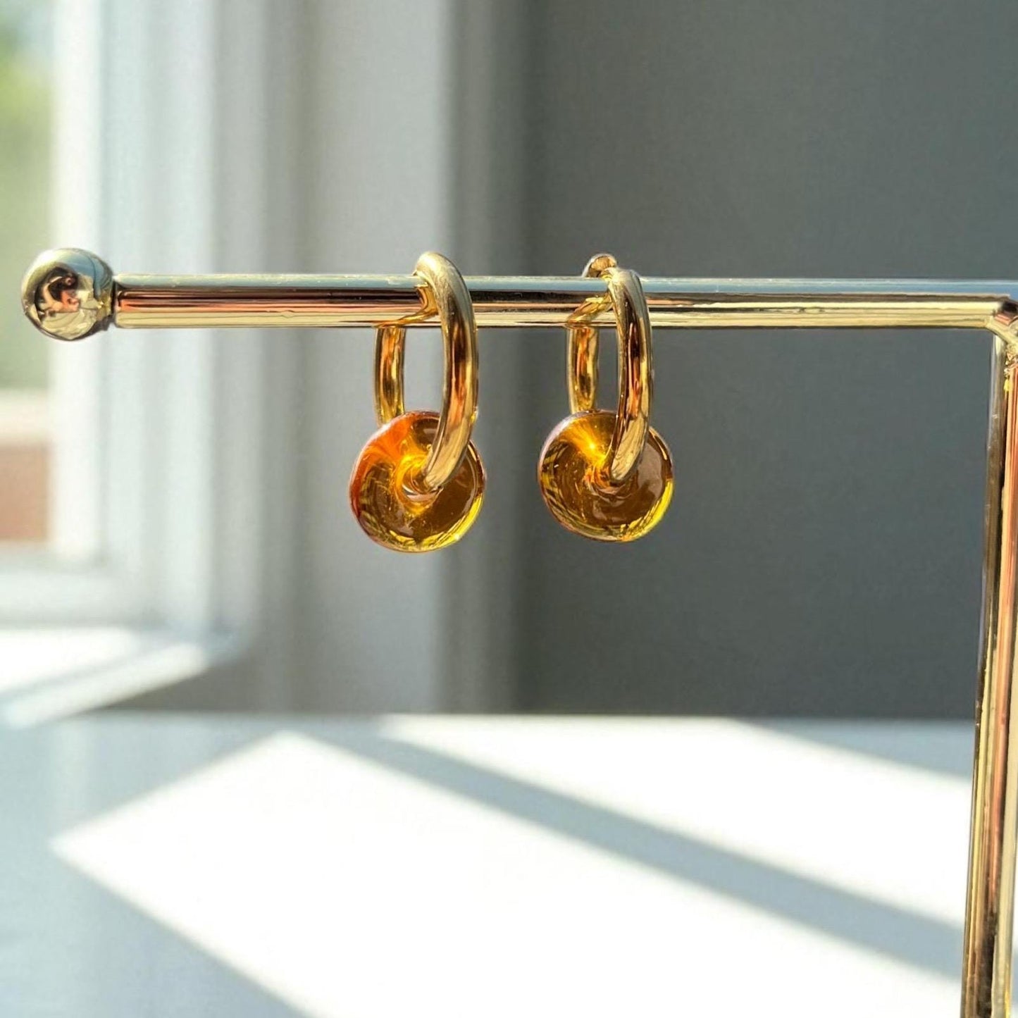 Gold hoop earrings with amber-colored stones on a gold stand.
