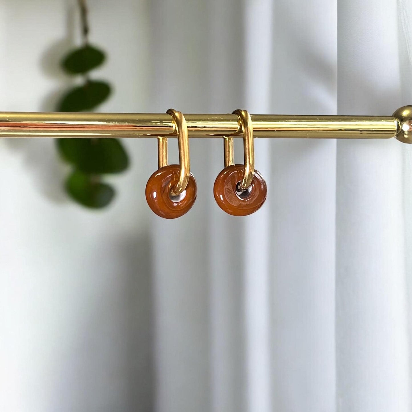 Gold curtain rod with brown circular hooks against a white curtain background