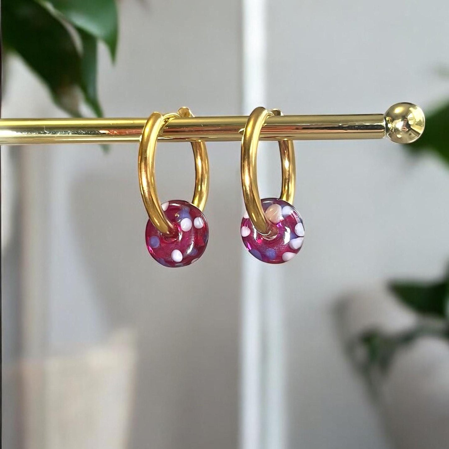 Gold hoop earrings with pink gemstones on a gold rod against a blurred natural background
