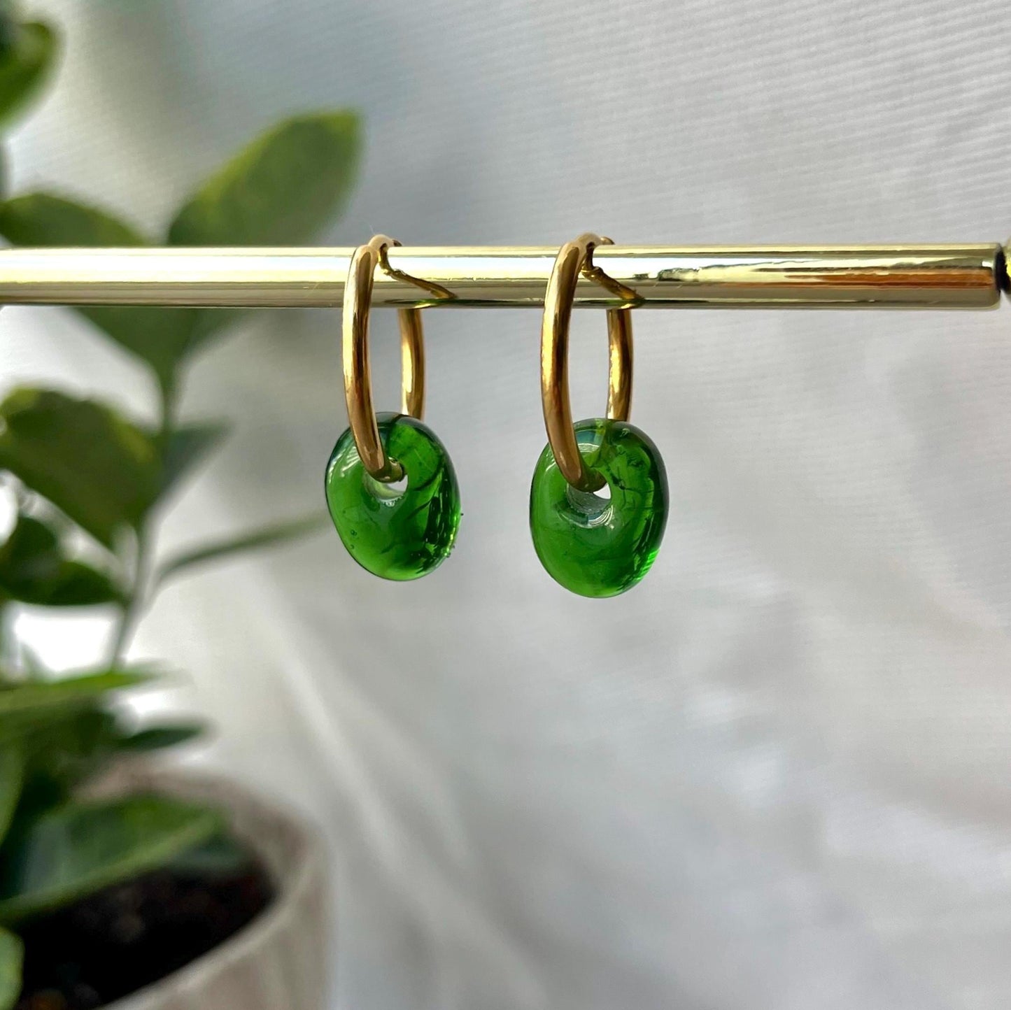 Gold hoop earrings with green circular charms on a blurred background