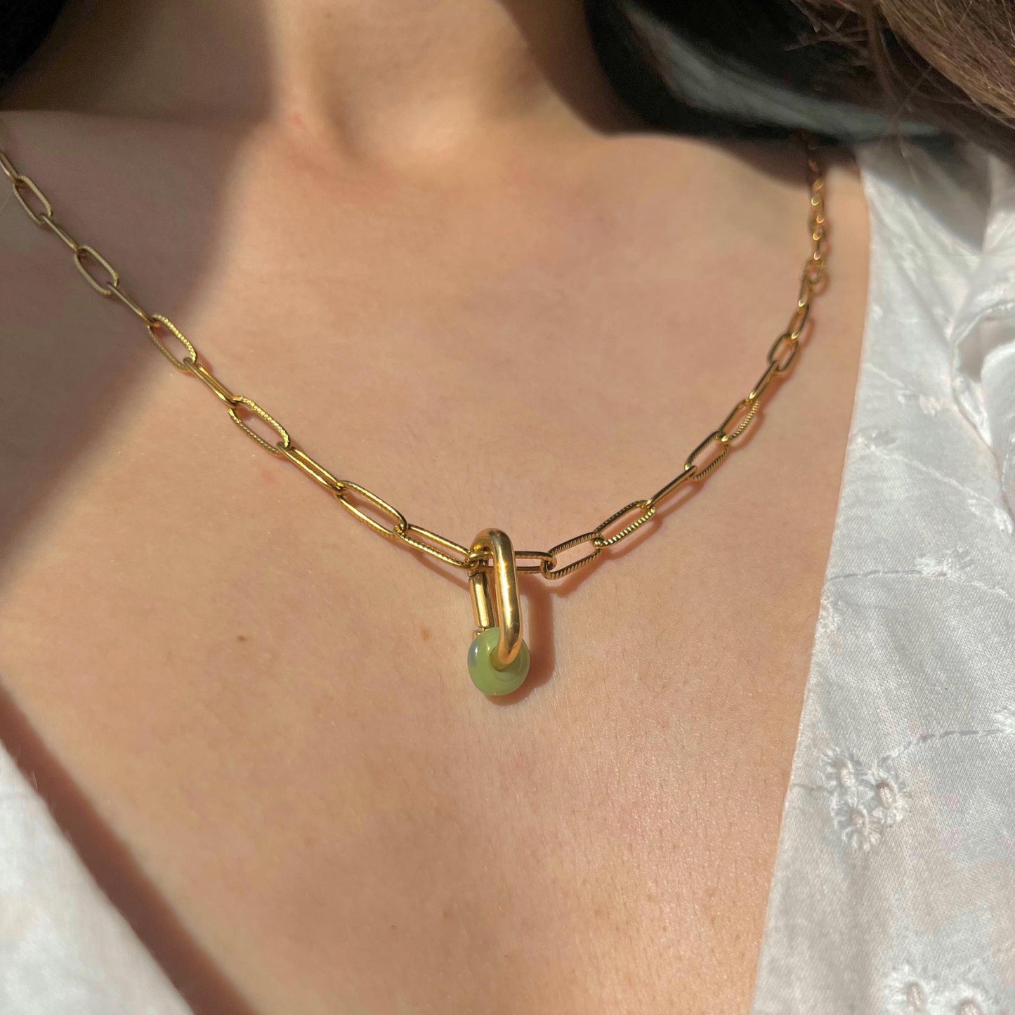 Gold chain necklace with a green pendant on a person's neck