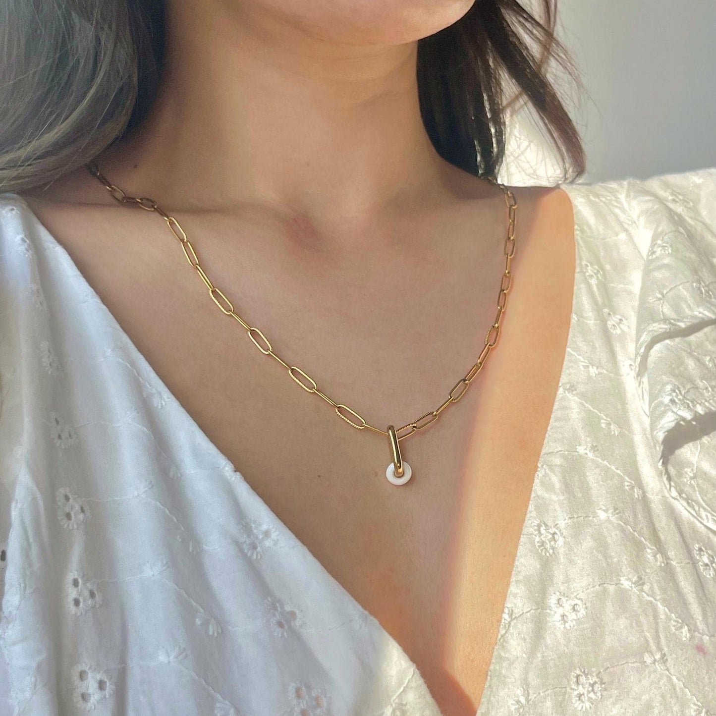 Gold chain necklace with a pearl pendant worn by a person in a white top.