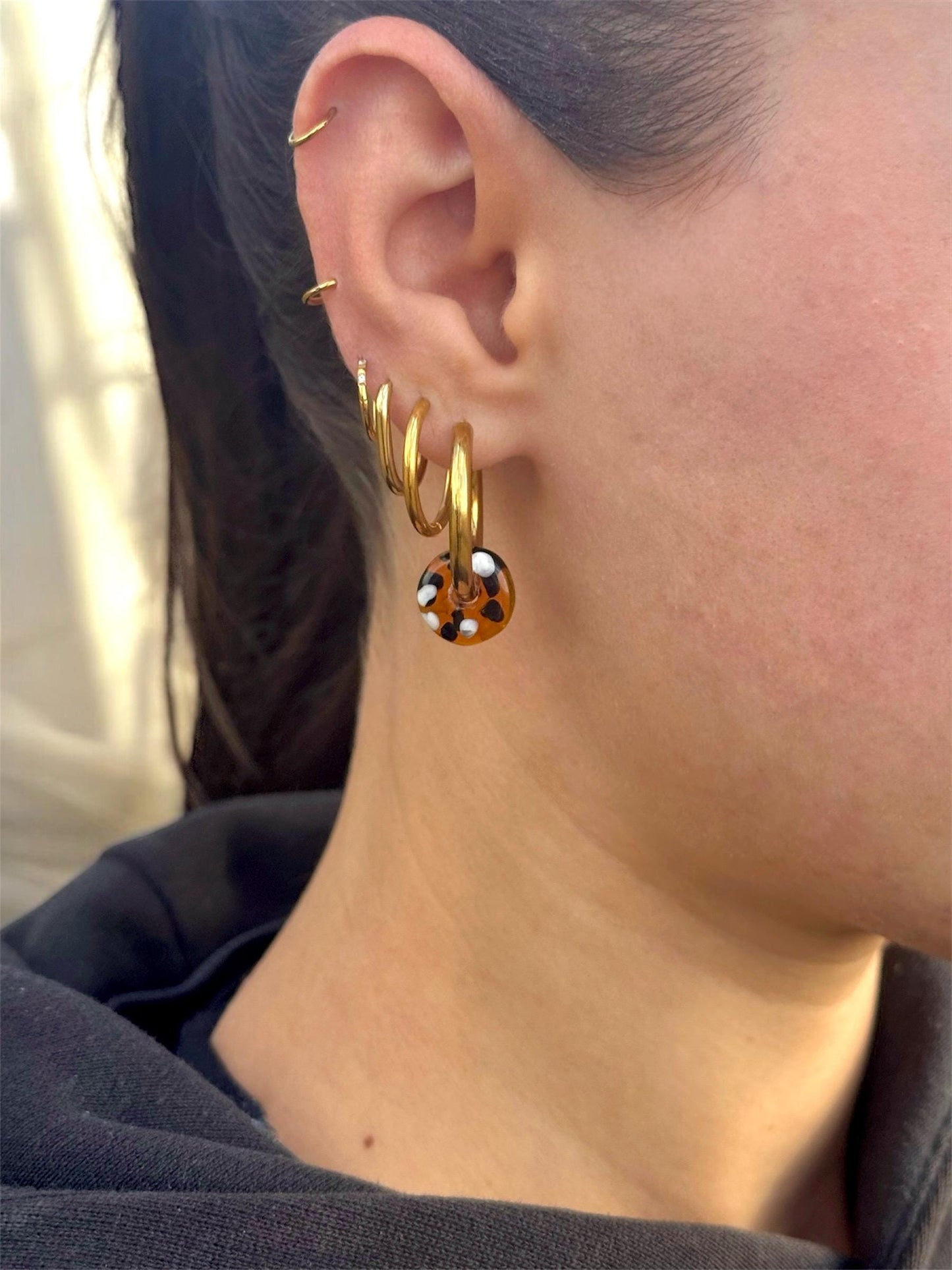 
                  
                    Close-up of an ear wearing gold hoop earrings with a blurred background
                  
                