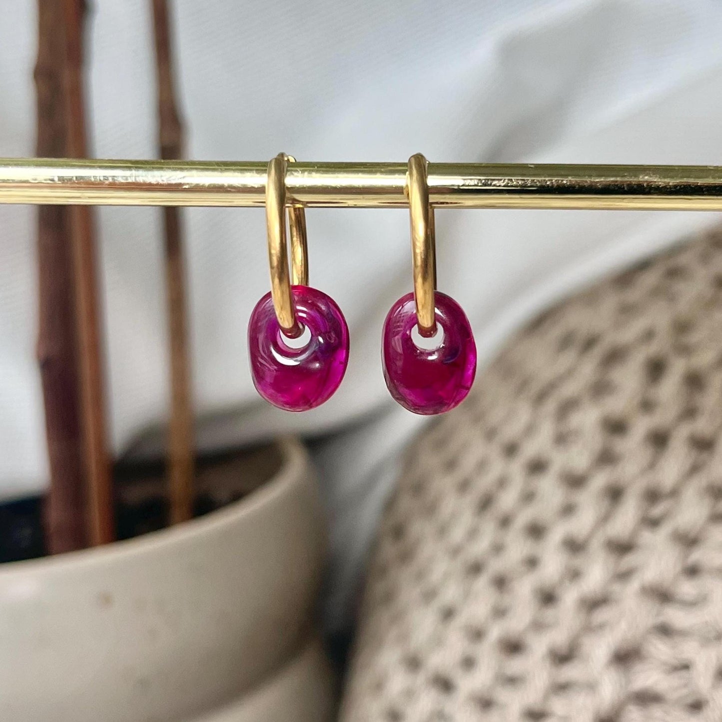 
                  
                    Gold hoop earrings with pink gemstones on a gold rod against a neutral background.
                  
                