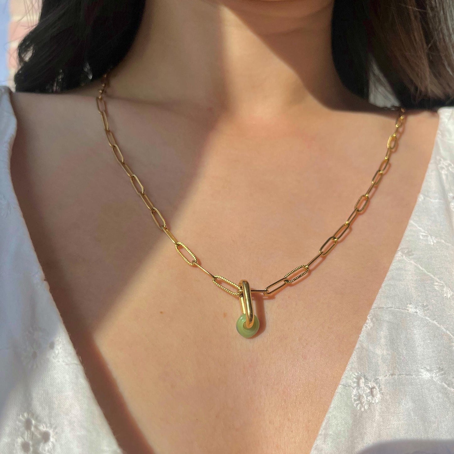Gold chain necklace with a green pendant worn by a person