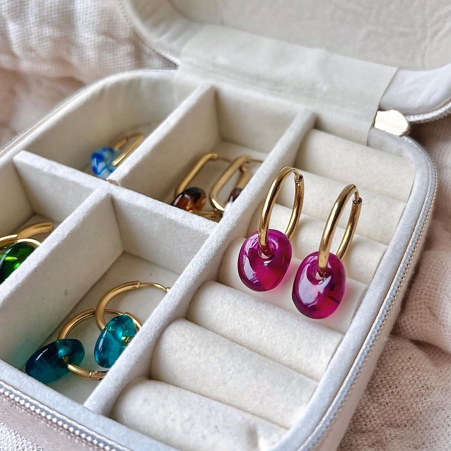 Gold hoop earrings with pink and blue gemstones in a jewelry box.