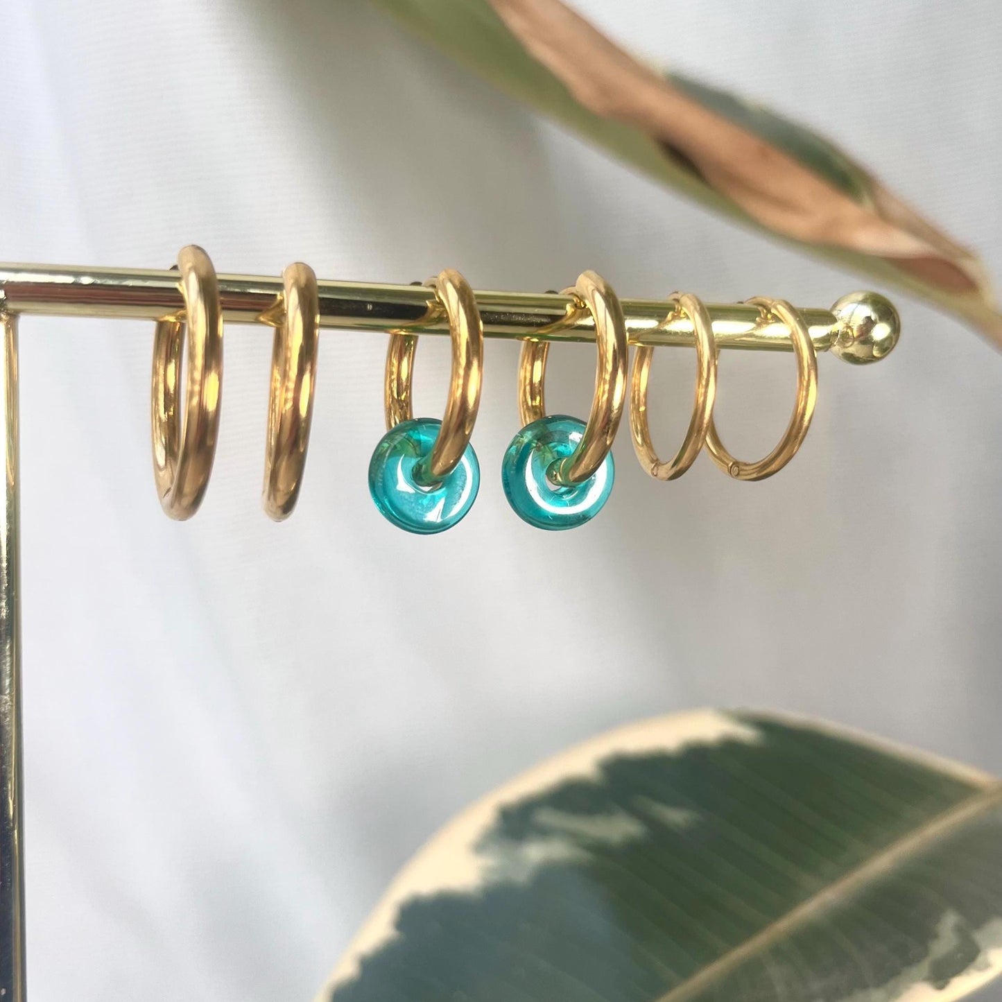
                  
                    Gold hoop earrings with turquoise stones on a gold stand with a leafy background
                  
                